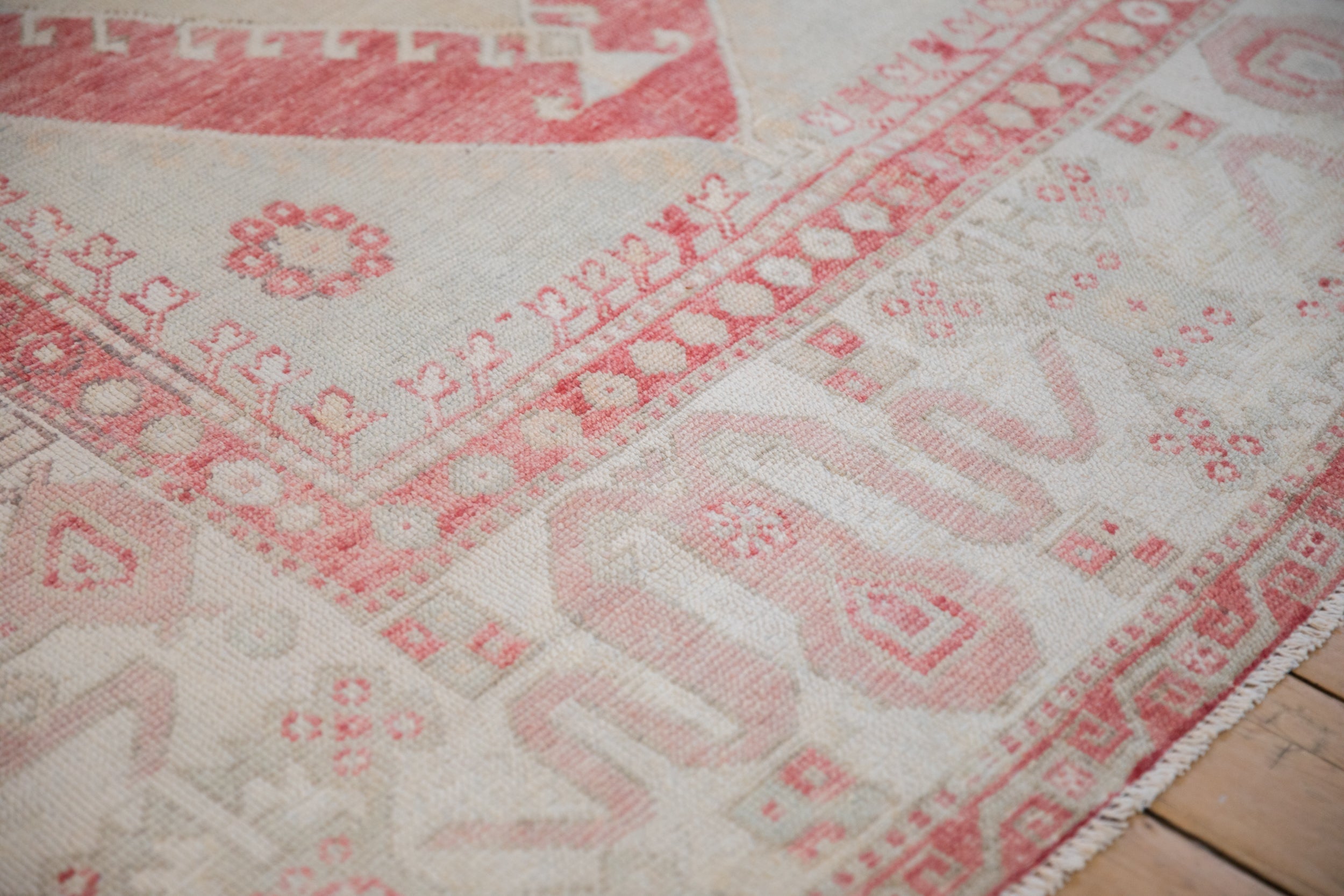 Expressive cloudband designs in faded red and ivory on a distressed vintage Turkish Oushak corner.