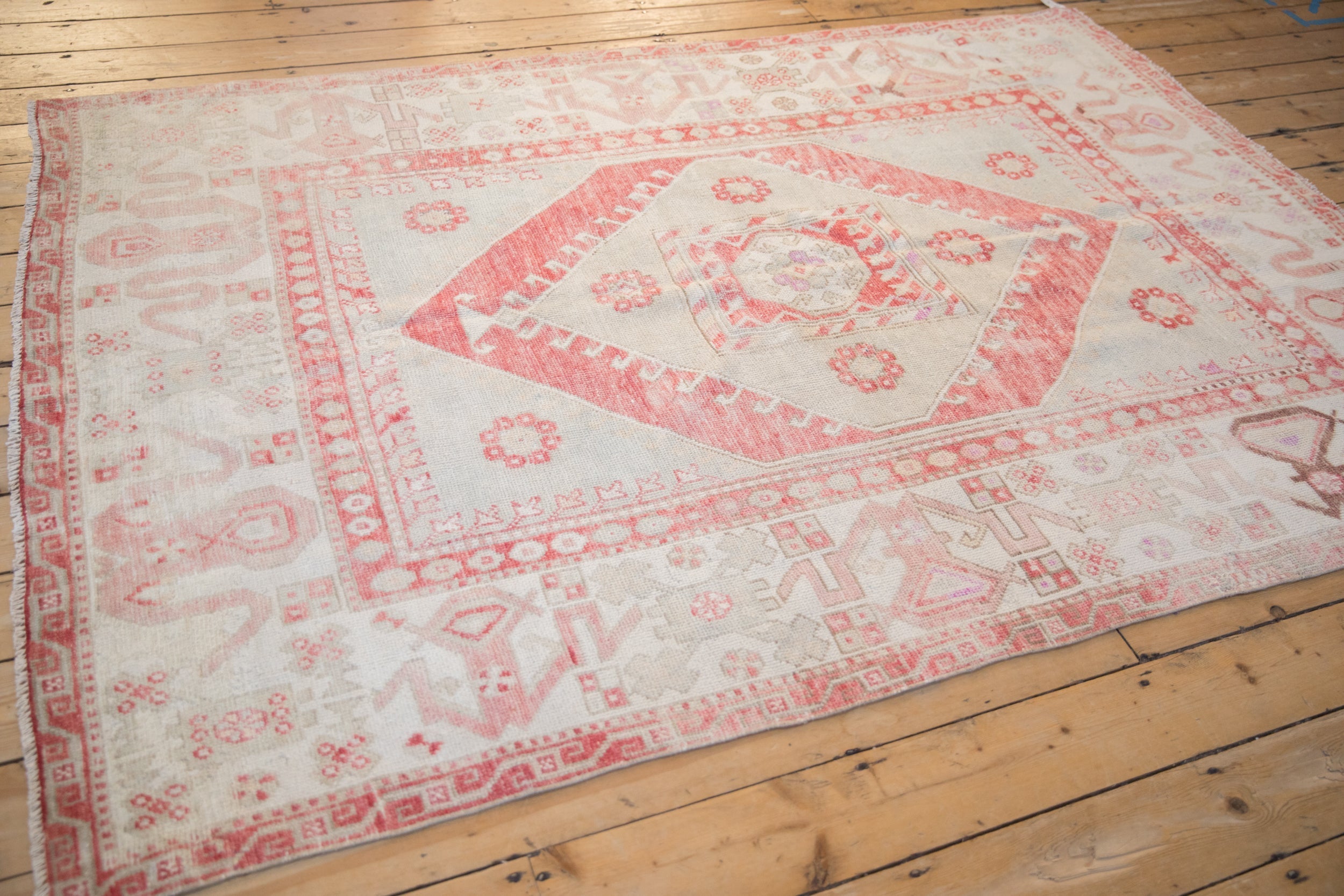 Distressed vintage Oushak carpet showing the ivory field and red cloudband border design from an angle.