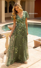 A woman stands by a pool wearing the Primavera 12193 long formal dress, a green, floor-length gown with floral beading and short flutter sleeves.