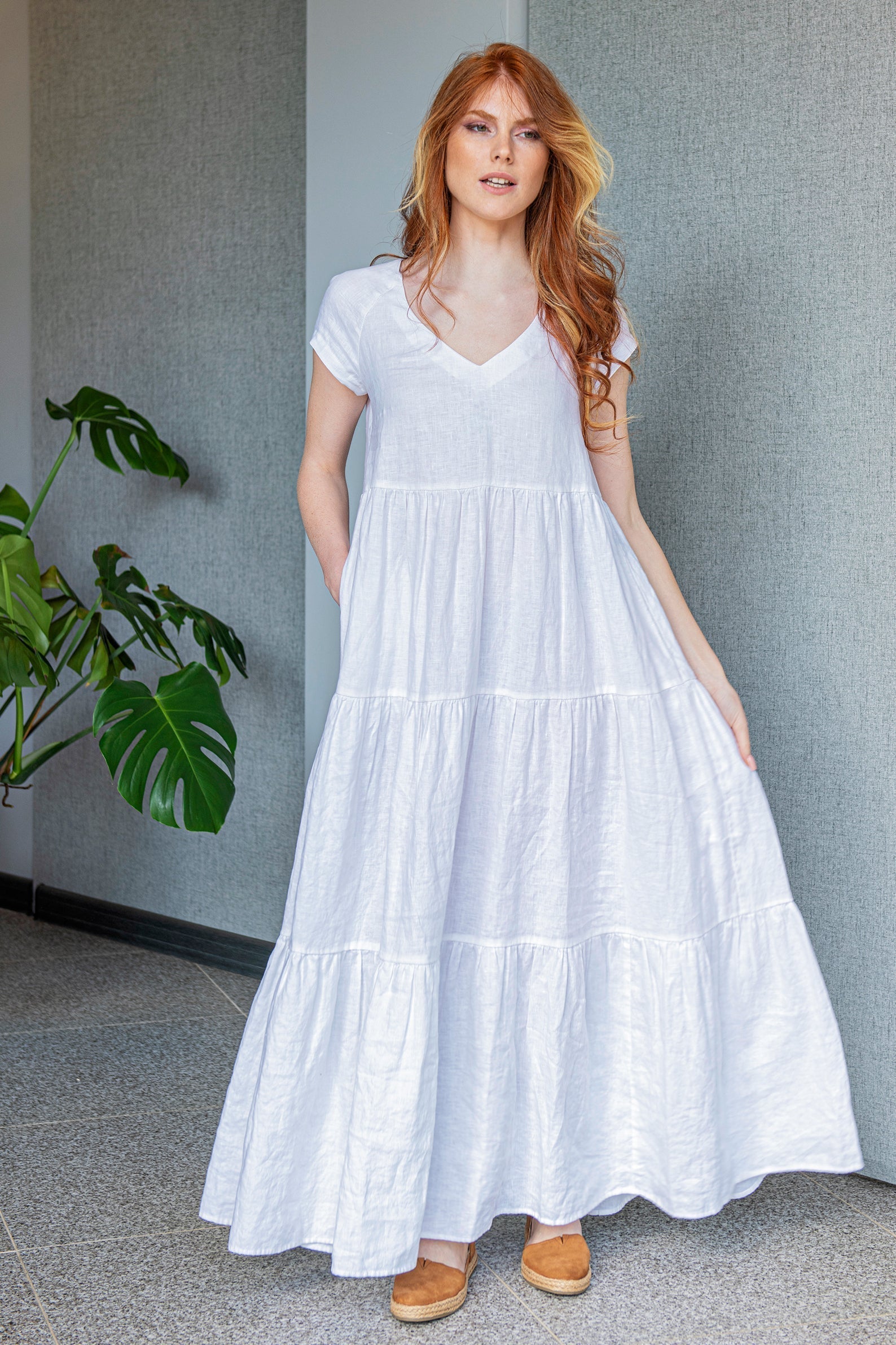 Woman wearing white bohemian linen dress with V-neck and tiered skirt standing indoors near plant