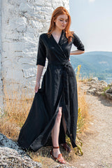Woman wearing black linen maxi dress with tie waist standing outdoors near stone wall