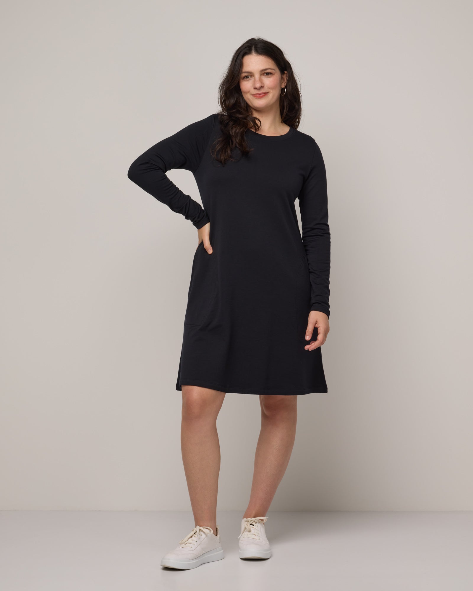Model wearing Eliza Swing Dress in Black. Eliza Swing Dress is a merino wool long sleeve, crew neck, knee length swing dress with pockets available in sizes XS-3X Regular, XS-3X Long.