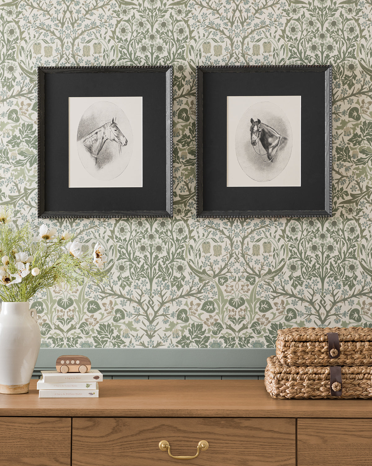 The Winnie framed horse portraits in black frames hang on a green floral wallpapered wall above a wooden dresser. A vase with flowers and stacked woven baskets sit atop, complementing the elegant Winnie wall art display by McGee & Co.