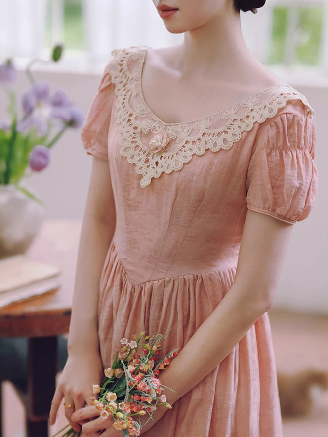 Close-up of a puff-sleeve soft pink dress with lace collar and floral accent, as the woman holds a delicate bouquet in a vintage setting.