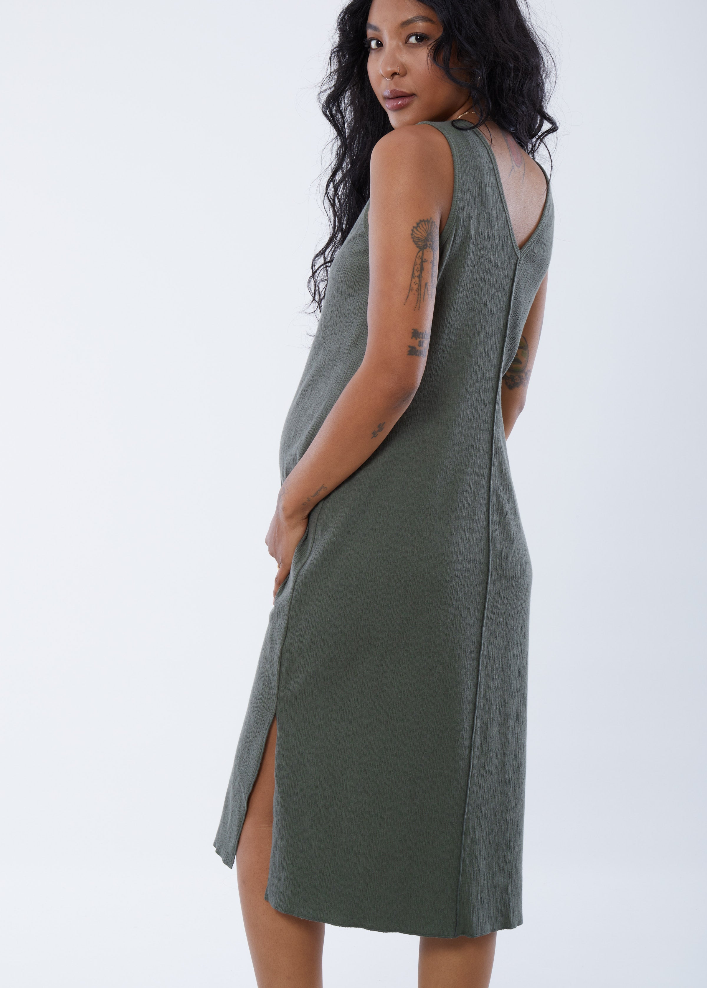 ||Pregnant woman wearing green v-neck, sleeveless dress on a plain background