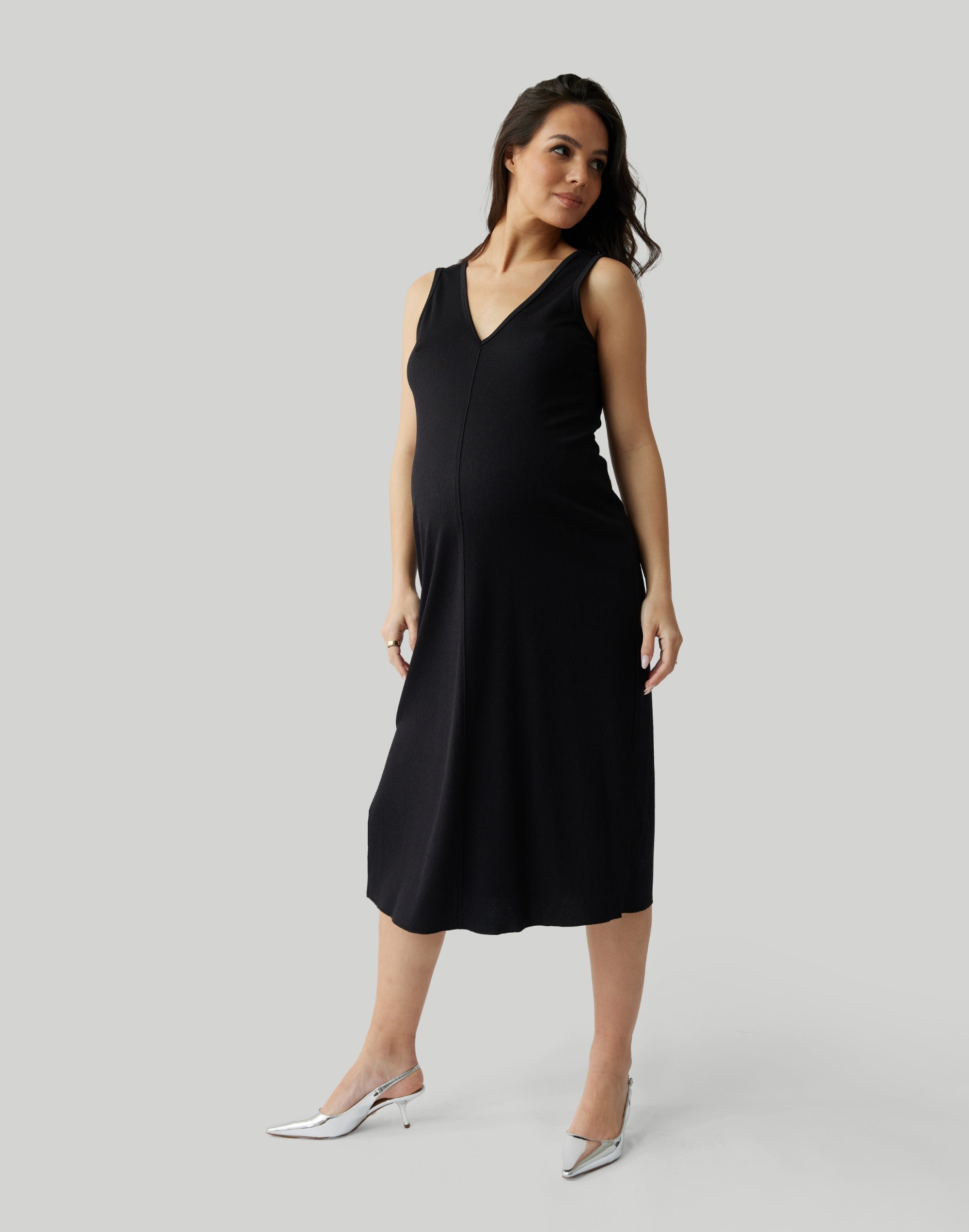 ||Pregnant woman wearing black v-neck, sleeveless dress on a plain background