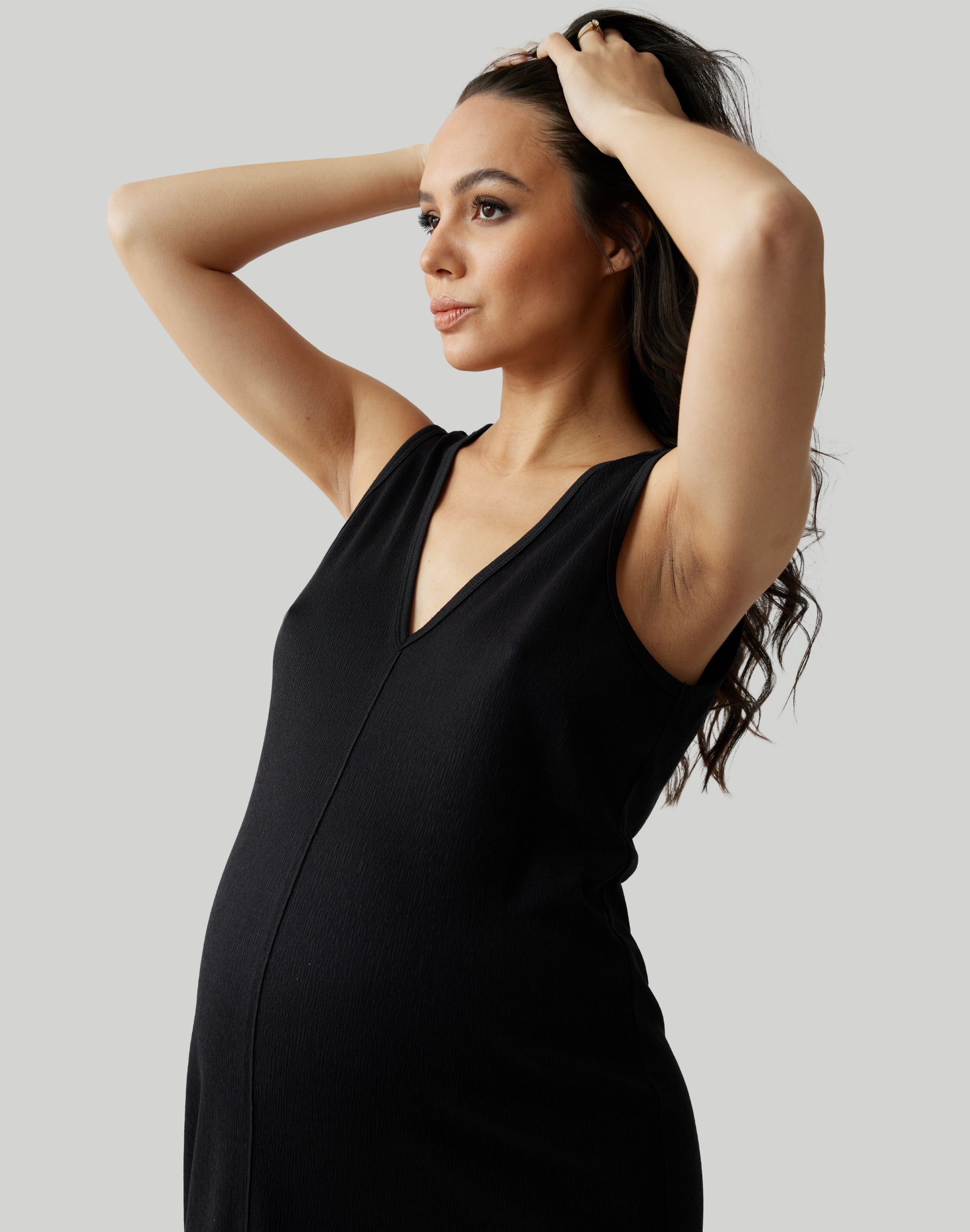||Pregnant woman wearing black v-neck, sleeveless dress on a plain background