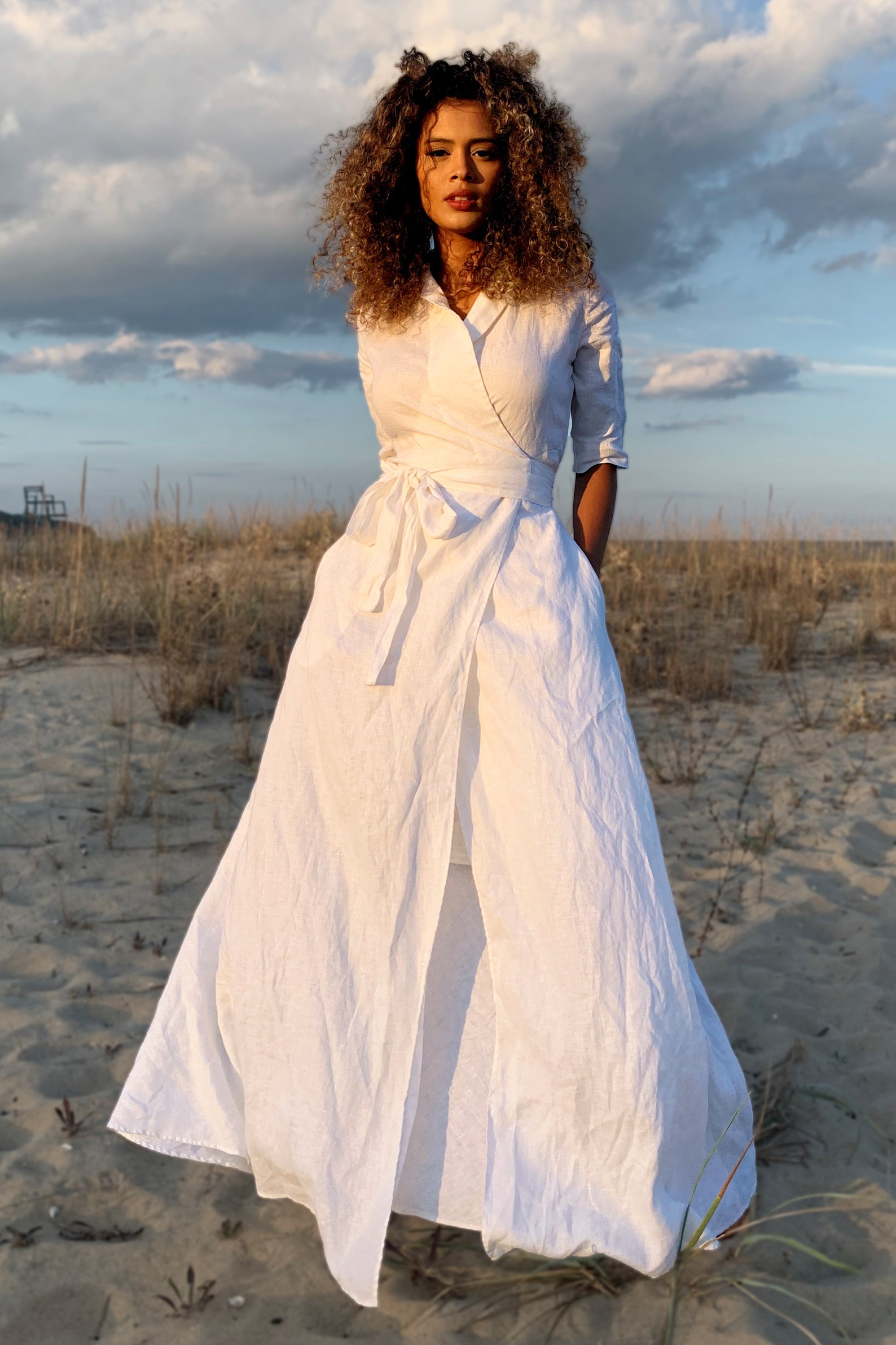 Woman wearing white maxi linen dress with tie waist on beach at sunset