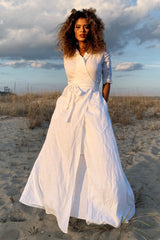 Woman wearing white maxi linen dress with tie waist on beach at sunset