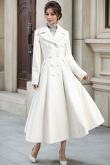 A woman wearing a white double-breasted long wool princess coat with a V-neck collar, button closures, and long sleeves.