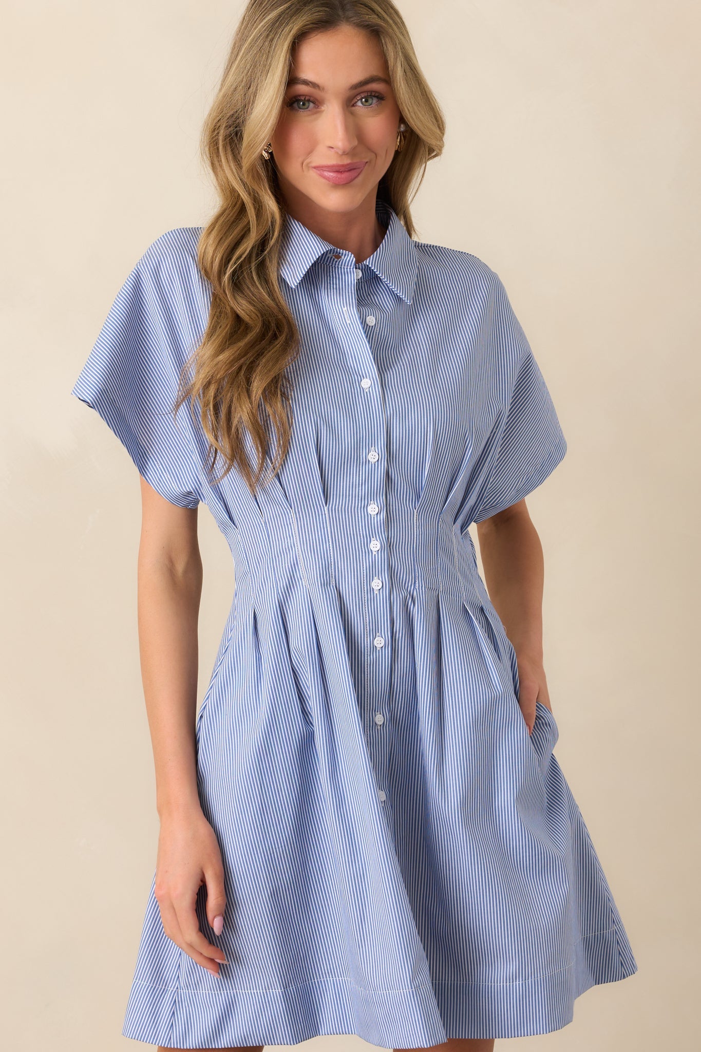 A cropped view of the blue stripe mini dress, emphasizing the pleated detailing and the flow of the fit-and-flare skirt. The vertical stripe pattern elongates the design.