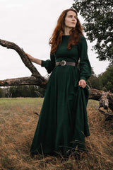 A person wearing a green linen maxi dress with long sleeves, standing next to a tree in an outdoor setting.