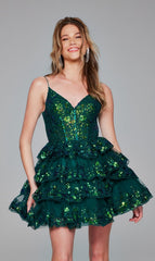A woman smiles at the camera in the Jovani 4382 Short Emerald Green Ruffle Hoco Dress, featuring sequins, thin straps, and ruffled details against a plain background.