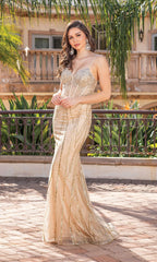 A woman poses outdoors in a Corset-Bodice Long Gold Prom Dress with thin straps and sequin embellishments. She pairs the shimmering, floor-length gown with large earrings, her wavy hair flowing amid lush greenery and a building backdrop.