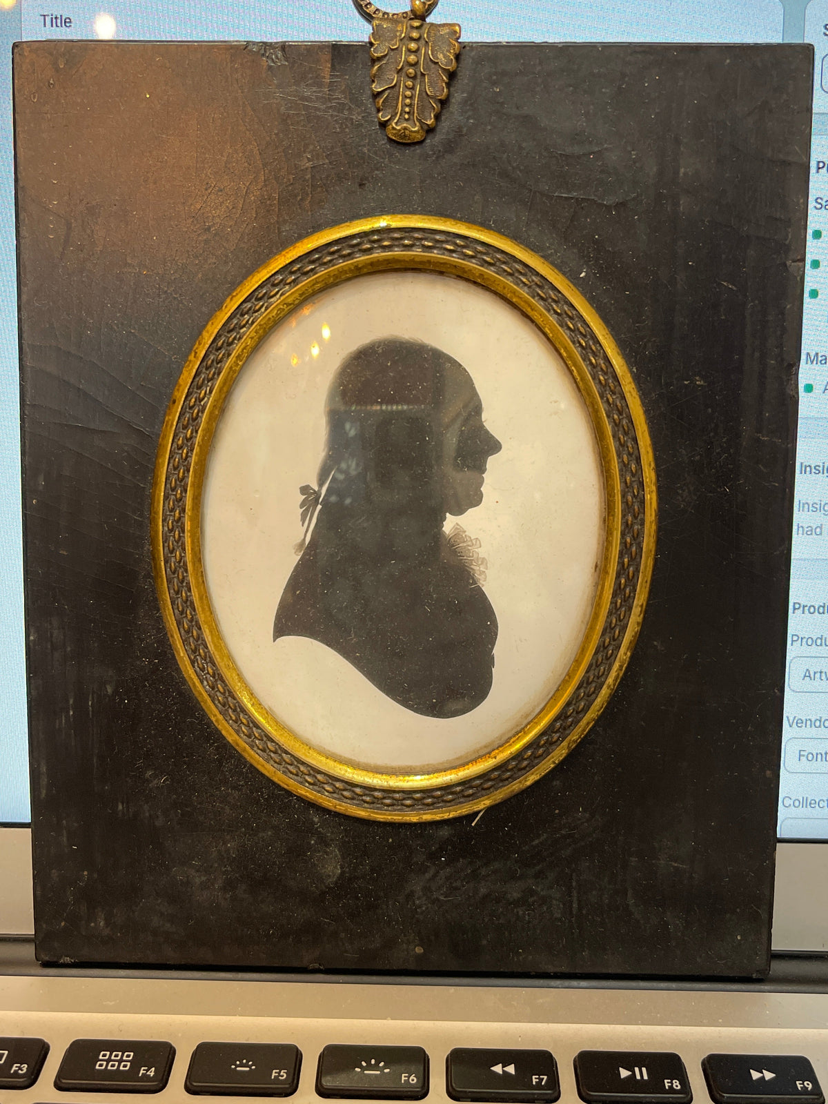 A framed silhouette portrait displayed on a table, featuring a black and white image of a person's profile with a decorative gold frame.