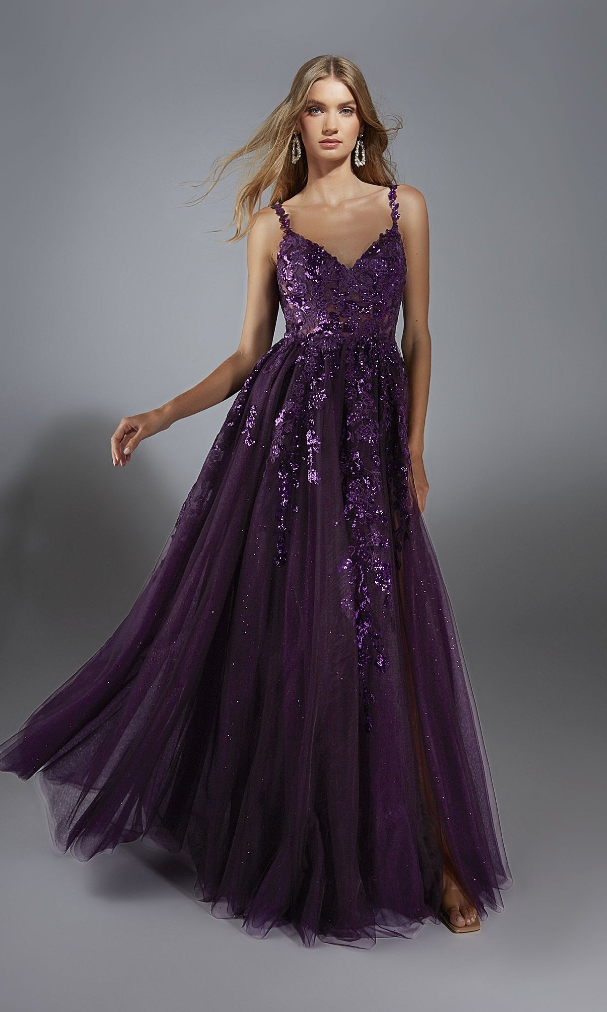 A woman in the Alyce 61891 long prom dress, which has lace appliques and a sleeveless, floor-length glitter tulle a-line skirt, stands against a gray background.
