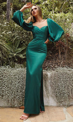 A woman stands outdoors in the Long Sleeve Long Wedding-Guest Dress 7482, an emerald formal gown with puffed long sleeves and a thigh-high slit—an elegant wedding guest option under $100.