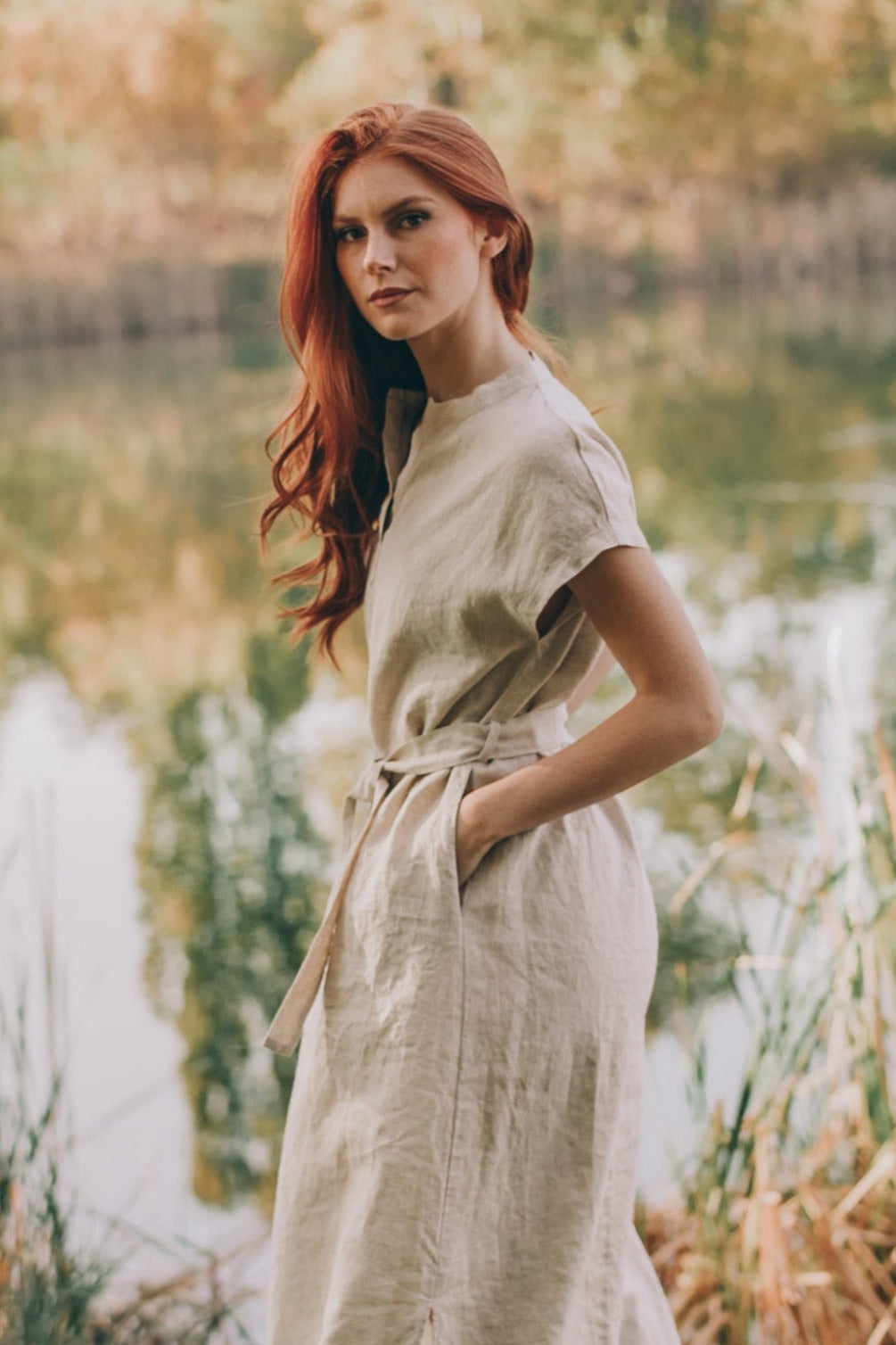 Woman wearing a relaxed linen maxi dress with tie waist standing outdoors near water and greenery