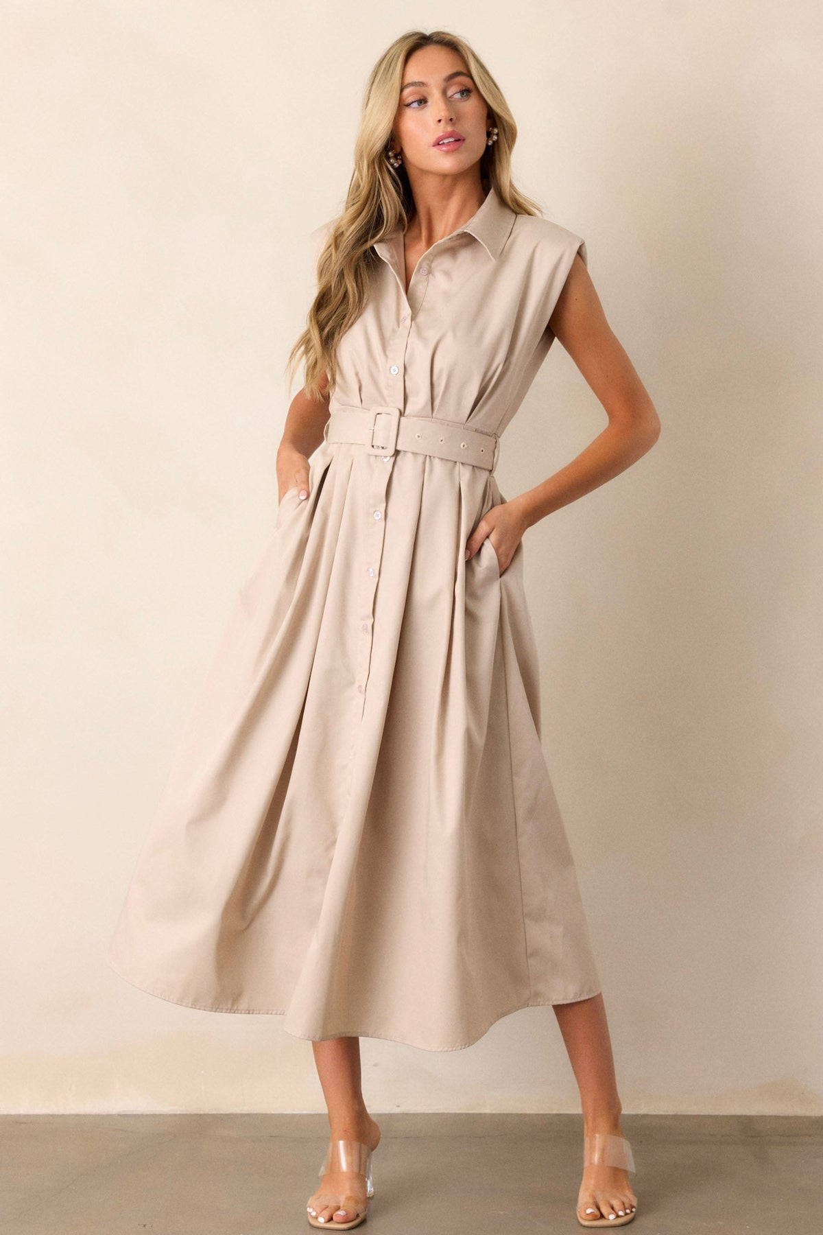 Movement  view of this beige dress that features built-in shoulder pads, a functional belt and a functional button front.