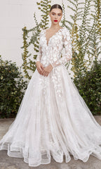 Someone stands outside in front of a greenery-covered white brick wall, wearing the LadivineA1067W Long Sleeve White Lace Bridal Gown, which features floral patterns and a deep V-neckline.