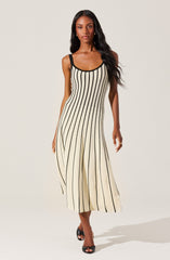 A woman is wearing a sleeveless, ankle-length dress with vertical black and beige stripes. The dress has black shoulder straps and black trim around the neckline and armholes. She is also wearing black high-heeled sandals.