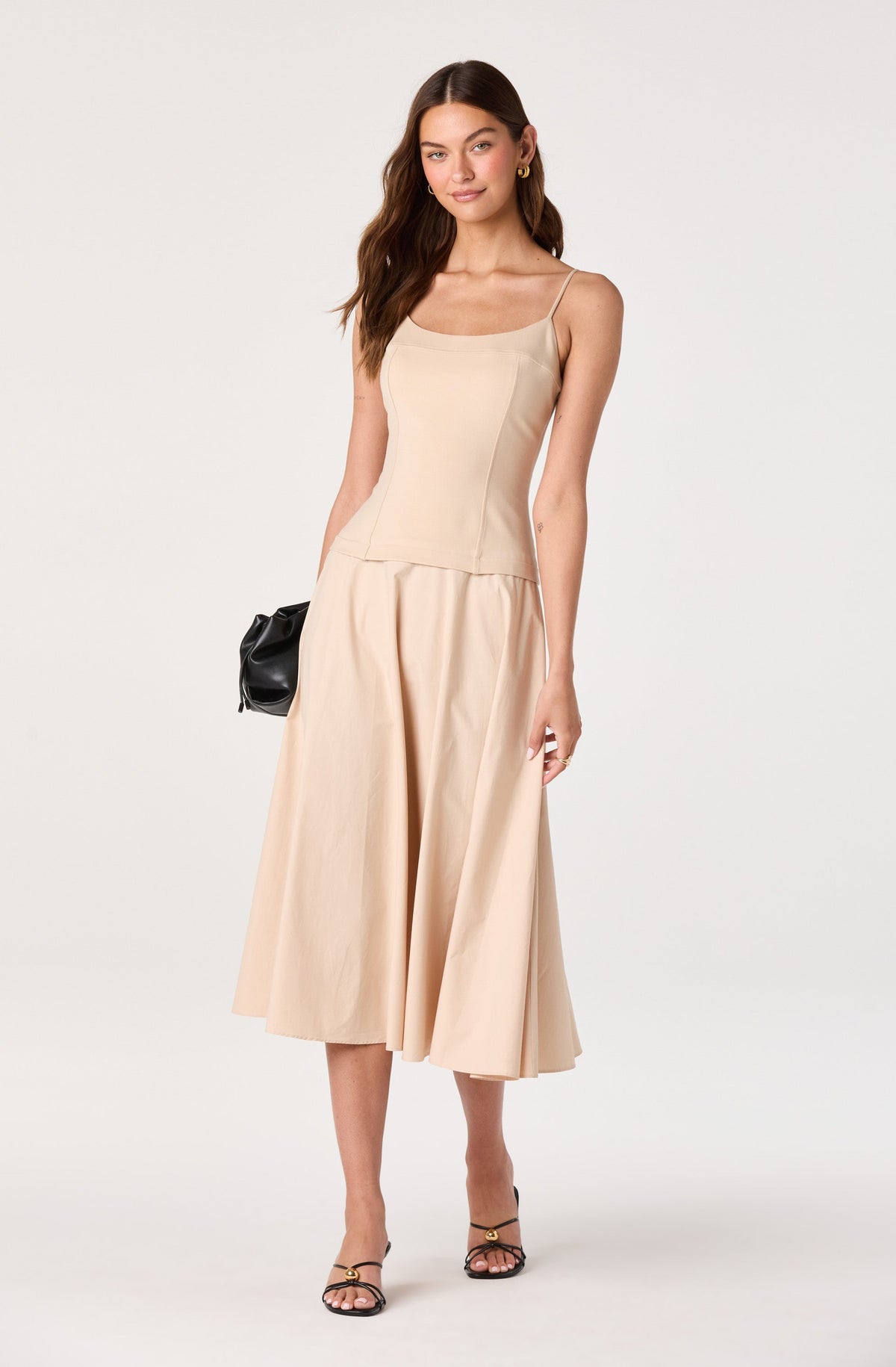 Woman in beige spaghetti strap top and wide-leg midi skirt, holding a black clutch.