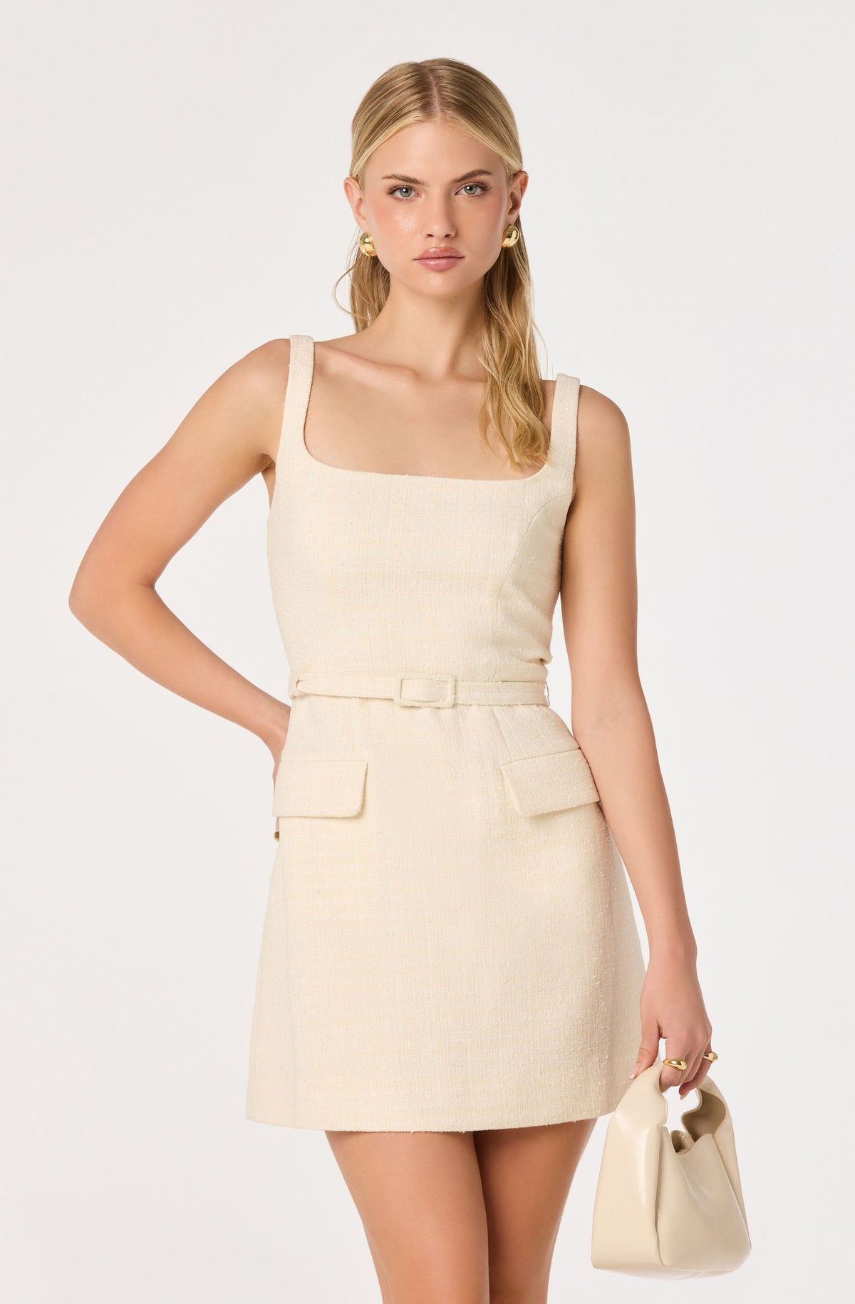 Woman wearing a cream sleeveless dress with a square neckline and matching handbag.