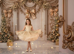 Young girl in a yellow dress standing in a decorated room with gold bows and Christmas trees.