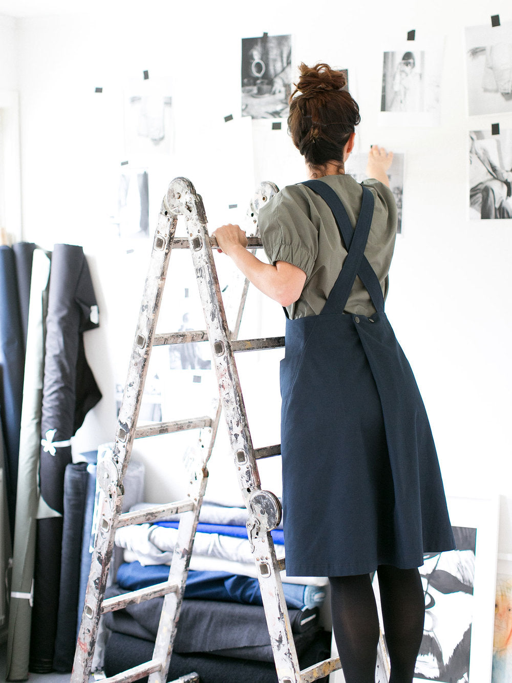 Woman wearing the Apron Dress sewing pattern by The Assembly Line. A pinafore style dress pattern made in denim, cotton twill or canvas fabric featuring cross over back straps, large front pockets and button pleat back opening.