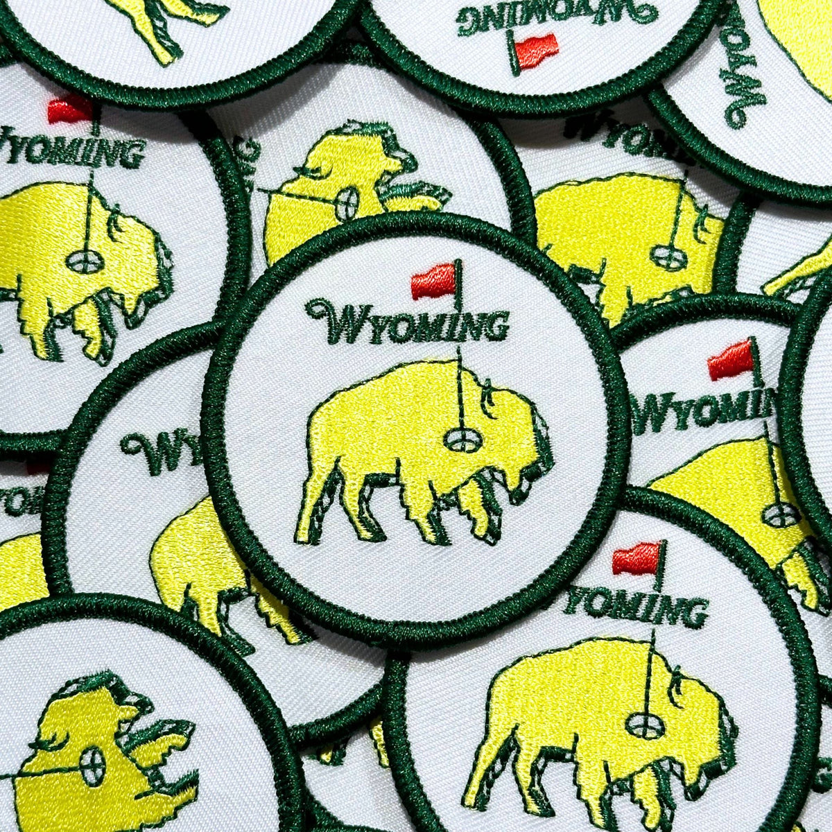 Circular embroidered patch. A neon buffalo in the middle acting as a golf green, with a hole and flag. 