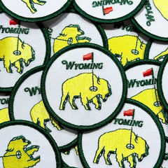 Circular embroidered patch. A neon buffalo in the middle acting as a golf green, with a hole and flag. 