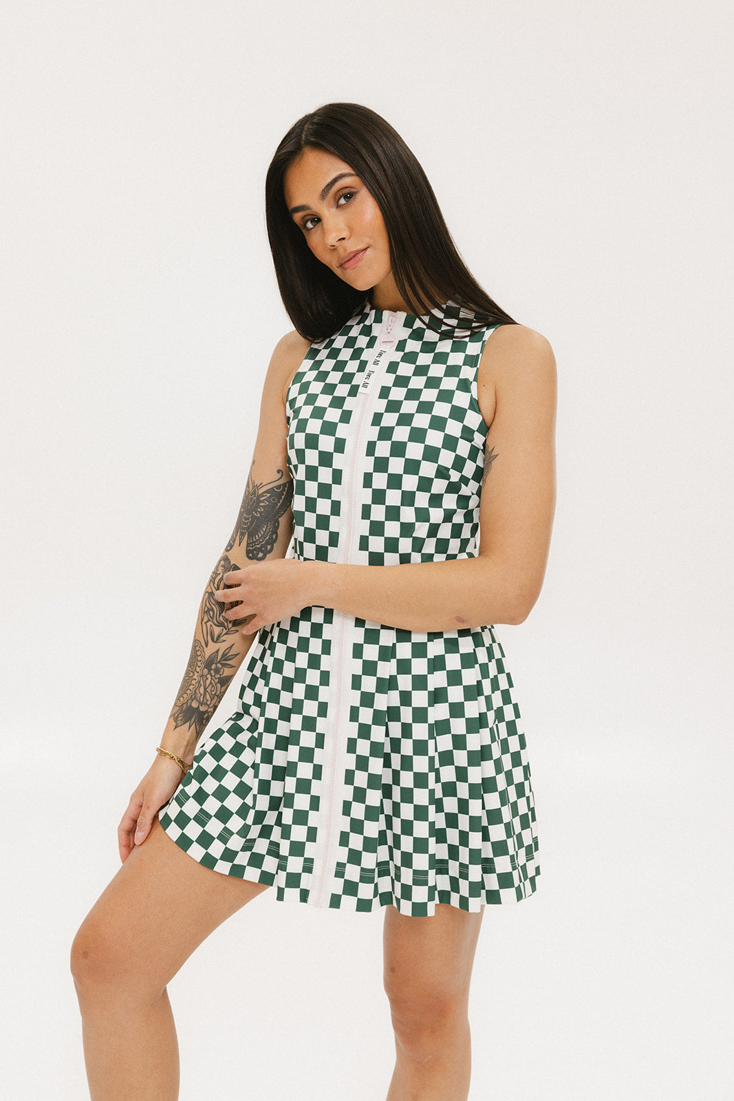 A model wearing a green and white checkered sleeveless dress with a zipper down the front and pockets.