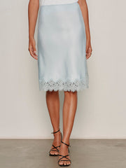 A person wears the Sanctuary Clothing effortless lace slip skirt in blue aura with black strappy heels, standing against a neutral background.
