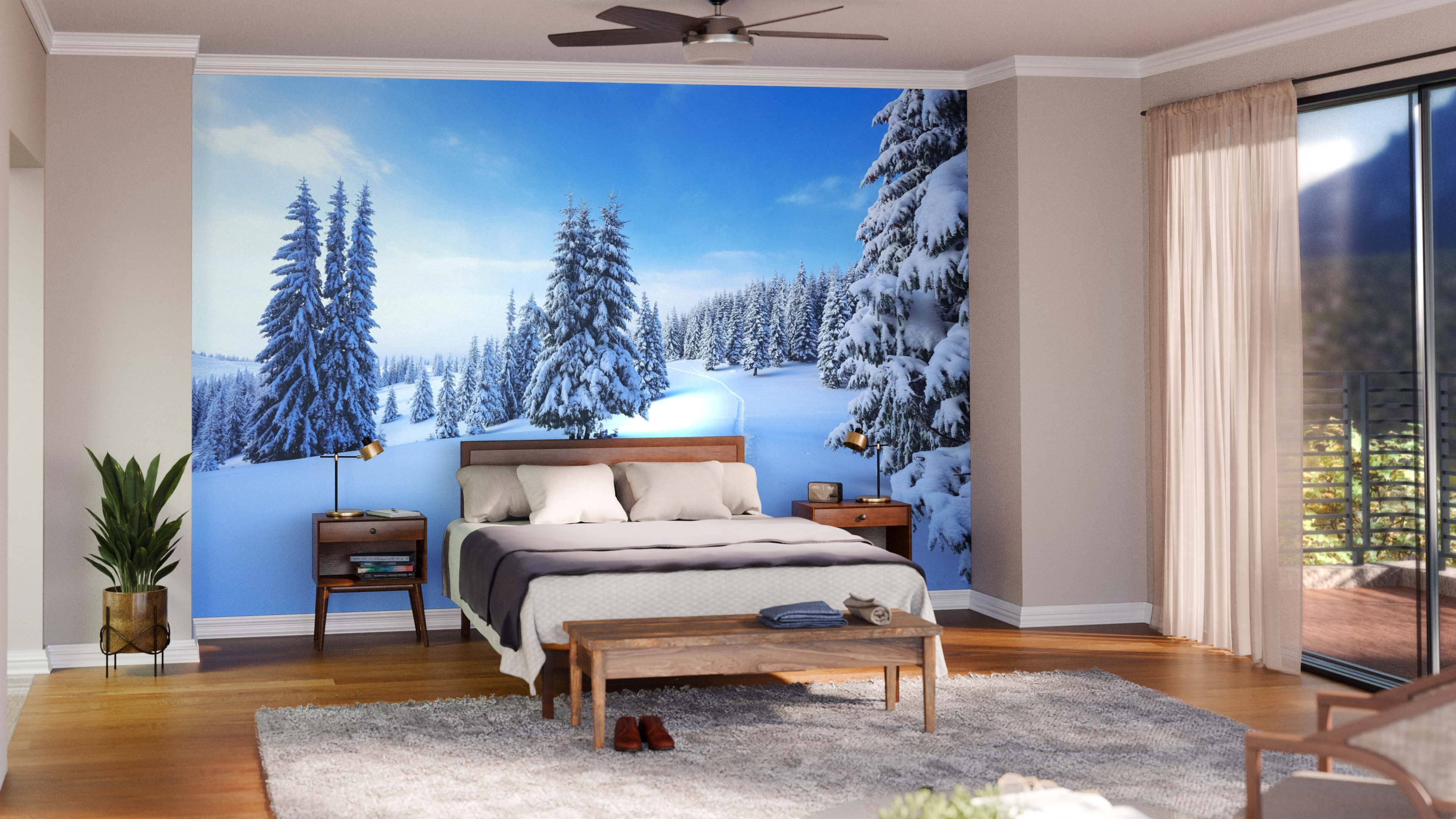 A cozy bedroom with a bed, wooden furniture, plants, and a gray rug features the Covered Winter Forest Wall Mural on the main wall. Sliding glass doors with sheer curtains fill the space with natural light.