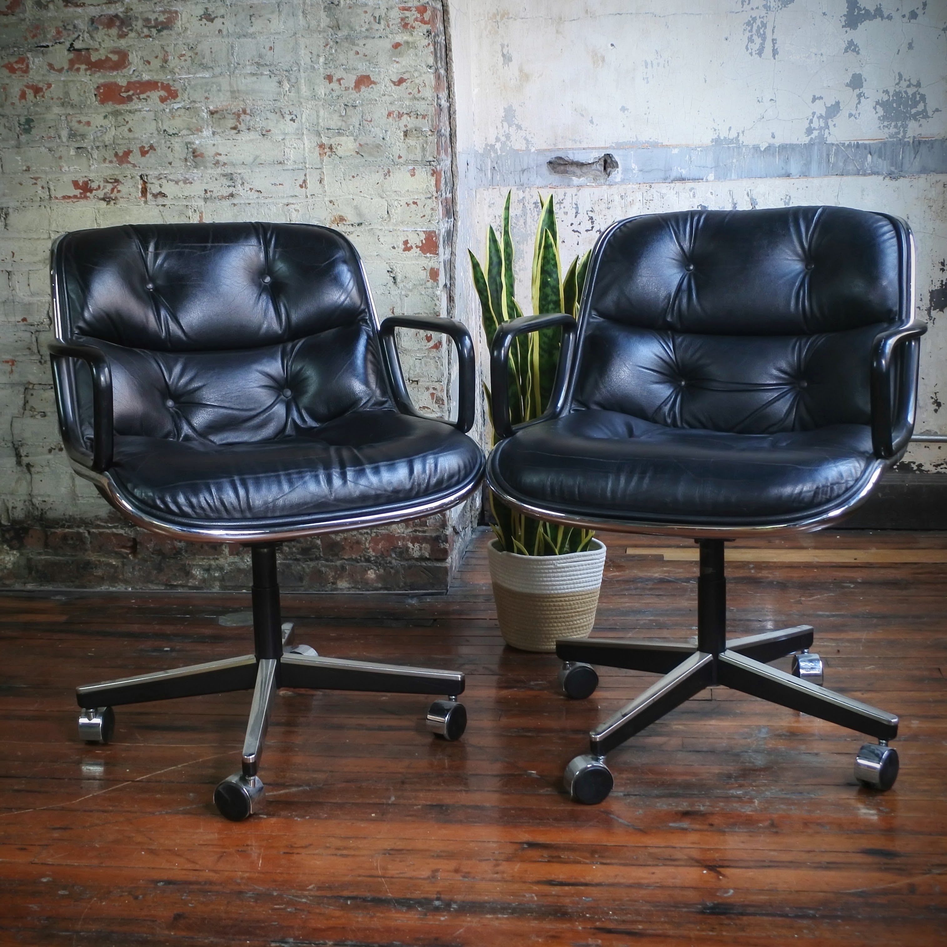 Two black leather office chairs on wheels in front of a brick wall.