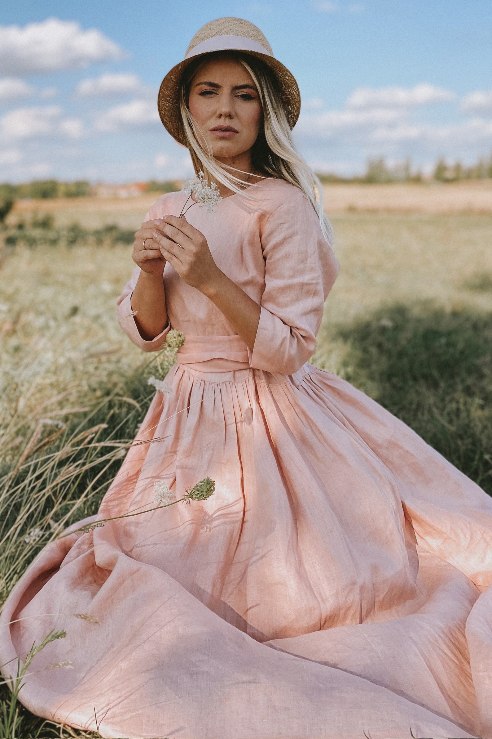 Woman wearing romantic linen summer dress with elbow-length sleeves and pleated bodice outdoors