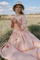 Woman wearing romantic linen summer dress with elbow-length sleeves and pleated bodice outdoors