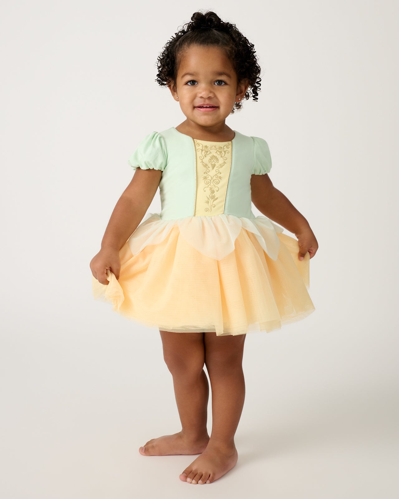 Standing toddler wearing the Disney Princess Tiana Dress with Bodysuit
