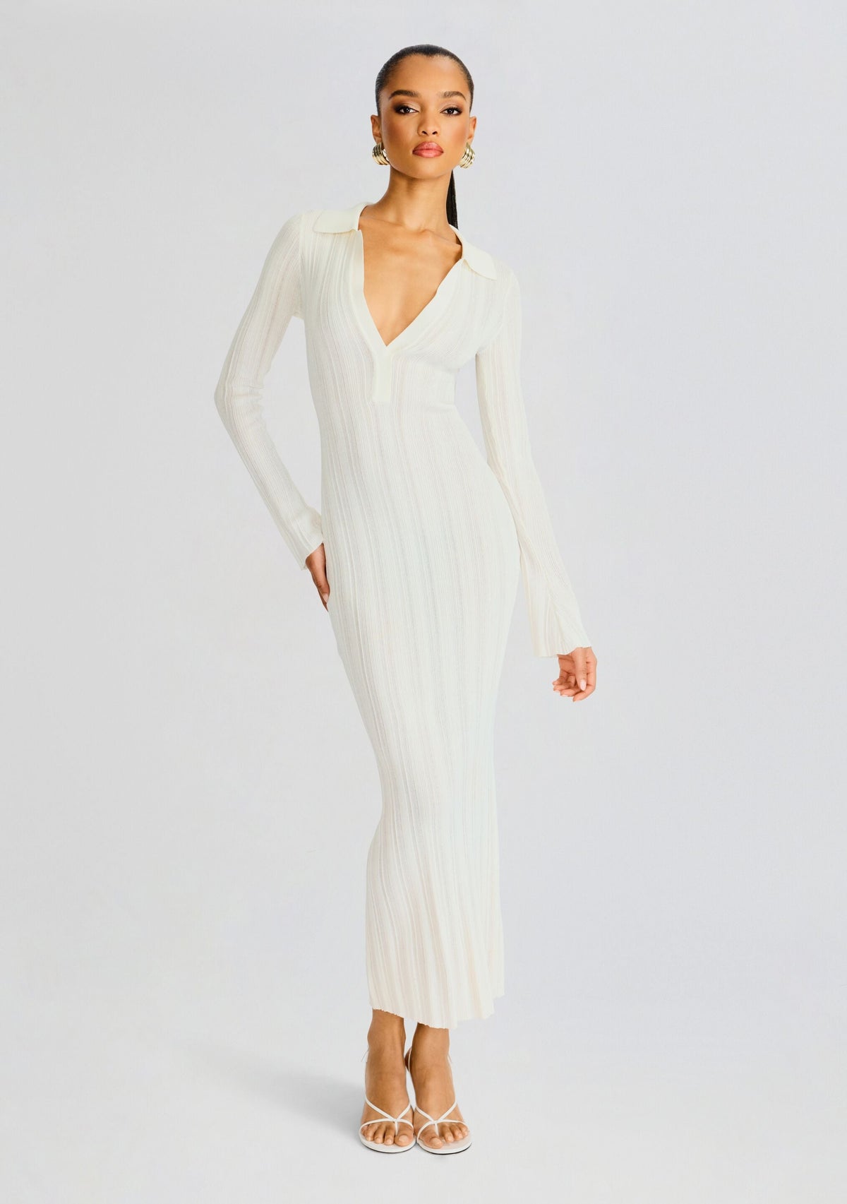 Full-length shot of a model wearing a white rib knit maxi dress with a deep V neckline and long sleeves.