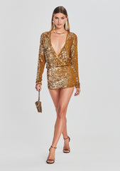 Model in a gold sequin crochet mini dress with long sleeves and a deep V neckline, holding a small gold clutch.