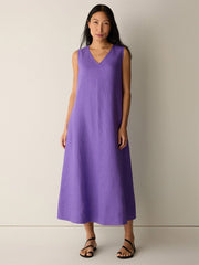 A woman stands against a plain background wearing the Eileen Fisher Organic Linen Easy Dress in Petunia and black sandals.