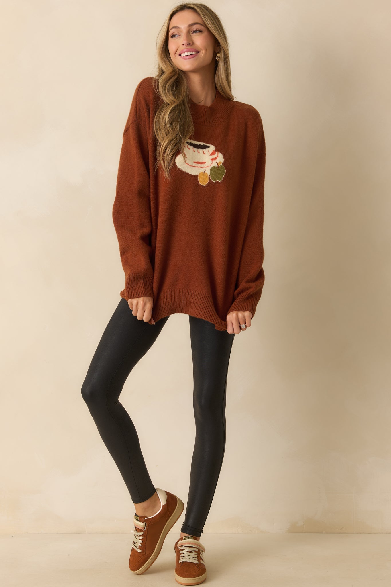 A front view of the rust brown sweater with intarsia knit coffee cup and apple graphic, classic crew neckline, and relaxed fit.