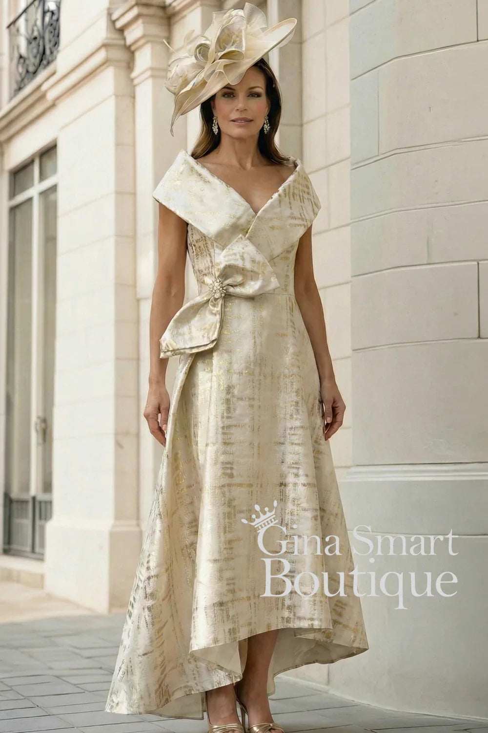 Gabriela Sanchez gold and Crudo metallic dress with dipped hem, statement waist bow, and matching hat – elegant Mother of the Bride outfit.