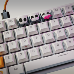 Mechanical keyboard with three Hollow Knight artisan keycaps in ghost mask shapes, showing neutral, blushing, and kissing expressions.