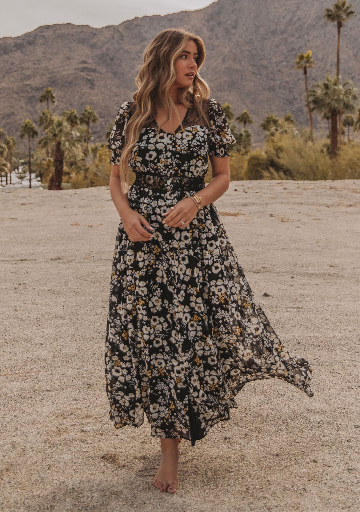 [Color: Black/Lemon] A model wearing a dreamy flowy bohemian maxi dress in a black and yellow floral print. With short puff sleeves, sheer lace accents, and a button front.