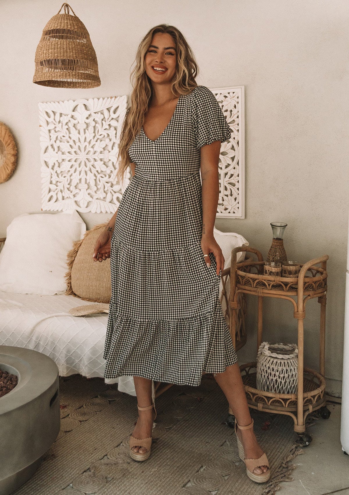 [Color: Black/Natural] A model wearing a black and white small checkered gingham mid length dress with short puff sleeves and an open back detail with button closure.