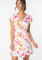 [Color: Ivory/Fuchsia] A model wearing a white and pink floral print mini wrap dress with short flutter sleeves and ruffled hemline.