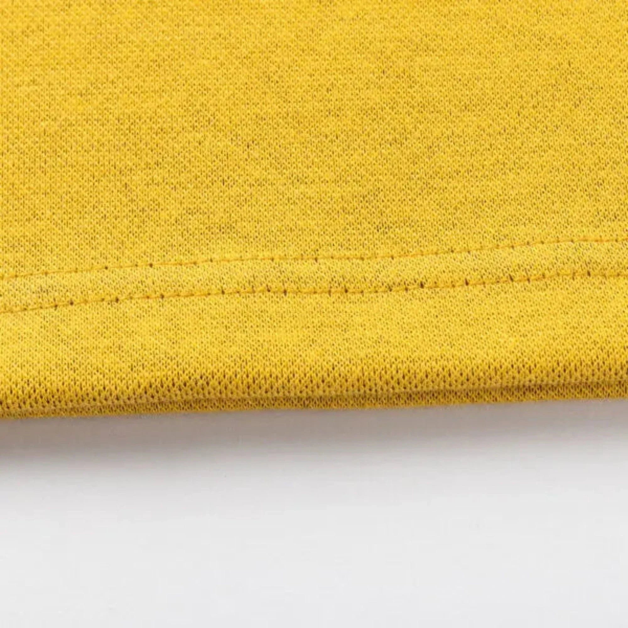 Close-up of a yellow fabric featuring edge stitching, reminiscent of Classic Sportswear's Limited Edition Hurricanes Super Rugby 25/26 Retro Jersey, against a white background.