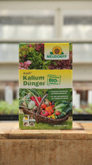 Eine 2 kg Kiste Neudorff Azet Kalium Dünger steht auf Holz und zeigt Gemüse und Blumen auf seinem natürlichen, biologischen Etikett. Geeignet für frostbeständige Pflanzen und ideal als Kaliumdünger für Obst und Gemüse.