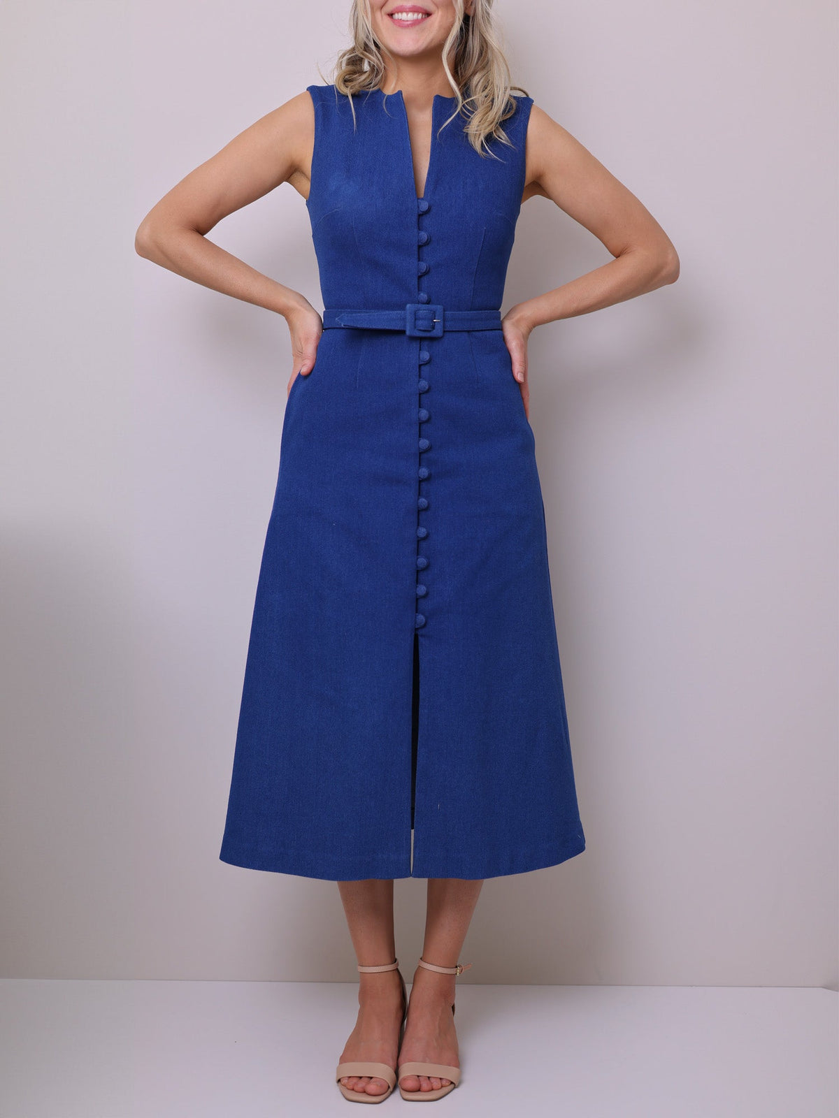 Sewing pattern for a sleeveless midi Dress in blue denim fabric, featuring a V-neckline, shank buttons, belt, and pockets.